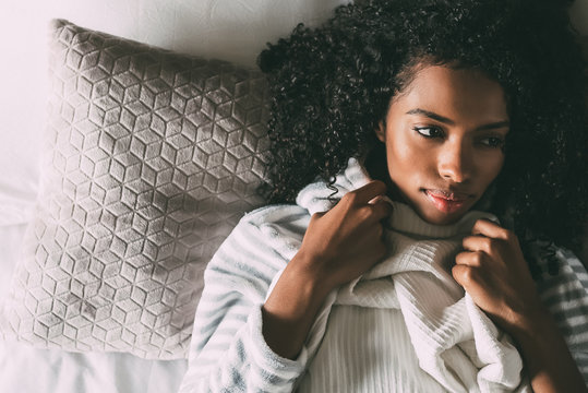 Beautiful thoughtful black woman with curly hair lying on bed looking away