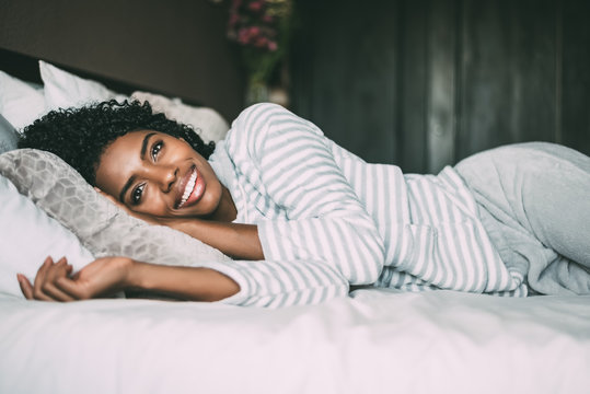 close up of a pretty black woman with curly hair smiling and lying on bed looking away