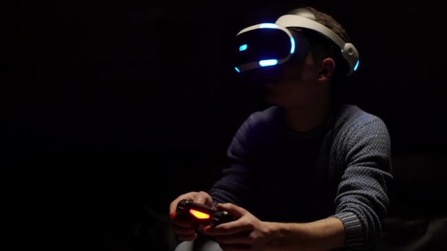 Portrait of game boy 20s involved in cyberspace as playing video simulation in virtual reality, using digital glasses and controller in dark room