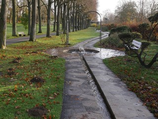 View into a spa park, with benches, paths with water,  trees in autumn