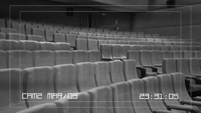 A CCTV security camera recording: red velvet seats in row and walls of a cinema or theater / theatre stage. Interior, angled shot.

