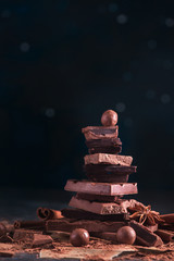 Stack of broken chocolate pieces on a dark background with copy space. Confectionery food...