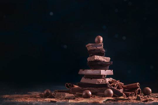 Stack of broken chocolate pieces on a dark background with copy space. Confectionery food photography in low key.