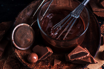 Close-up of chocolate glazing in a glass cup with a whisk. Cocoa powder, cinnamon and other spices on a black background. Macro food photography with copy space.