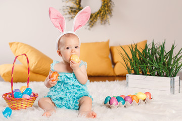 Cute adorable Caucasian baby girl in blue green romper wearing bunny ears sitting in studio. Kid child playing with Easter colorful eggs celebrating traditional holy Christian holiday.