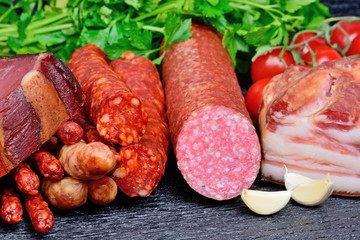 Prosciutto, dried sausages, salami and bacon with cherry tomatoes on a wood table