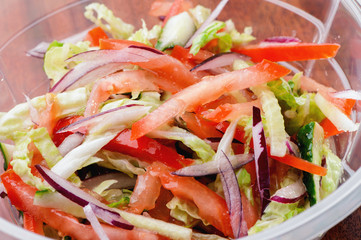 Fresh vitamin vegetable salad in plastic container close-up with chopped tomatoes, red pepper,  radishes,  cucumbers  and lettuce leaves on table 

