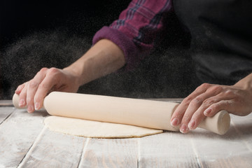 Chef roll out the dough on the working surface. Black background