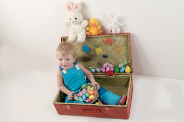 Little blond kid boy coloring eggs for Easter holiday in domestic room, indoors. Child holding basket with painted eggs. Child having fun and celebrating feast with easter toy bynny