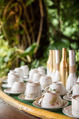 Vintage Tea Cups and Saucers Set out on a Table with Green Tropical Trees and Foliage in the Background