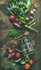 Winter vegetarian food cooking ingredients. Flat-lay of seasonal vegetables and fruit, beans, cereals, kitchen utencils, dried flowers, olive oil over wooden background, top view, vertical composition