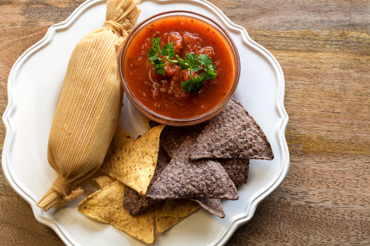 Tamale with hot tomato sauce and white and blue corn tortillas on Wooden table