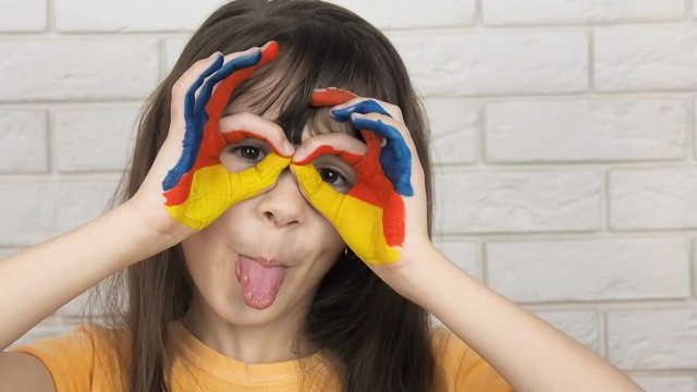 Child in paint. Funny child shows thumbs up glasses.