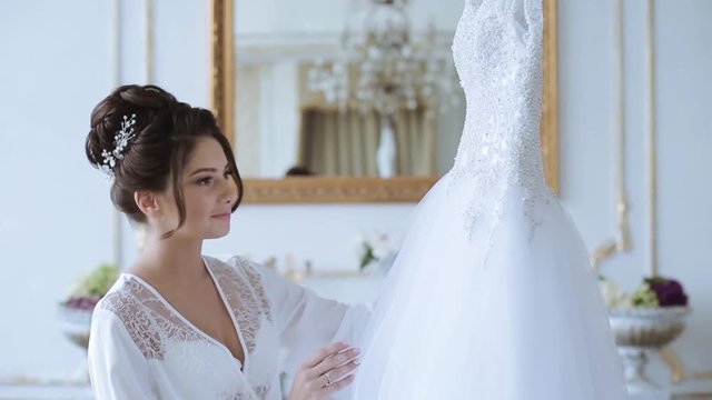 Beautiful bride in robe is watching a wedding dress