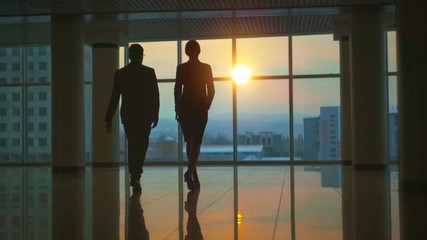 The man and woman walking in the office hall on a sunset background. slow motion - Powered by Adobe