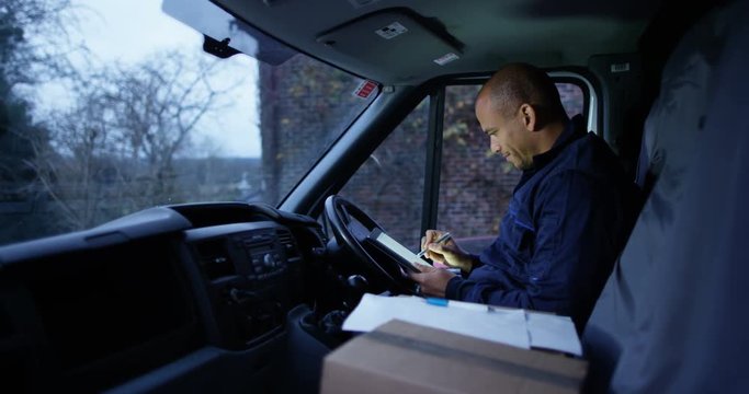 4K Portrait delivery driver smiling to camera, sitting in vehicle checking his paperwork
