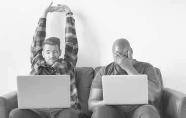 Two men using laptop sitting on sofa
