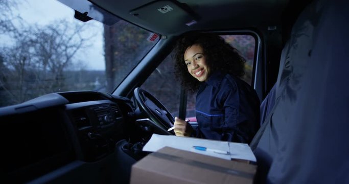 4K Female delivery driver smiling to camera, sitting in vehicle with parcels on seat