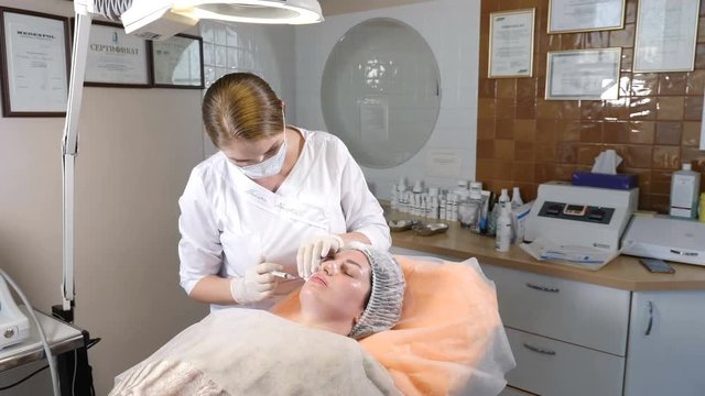 Beauty clinic. Beautician in gloves making face aging injection in a female skin. A woman gets beauty facial cosmetology procedure. Botox. collagen injections. Shot in 4k