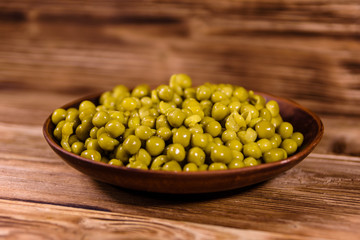 Ceramic plate with canned green pea on wooden table