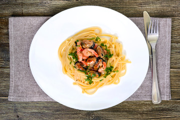 Pasta tagliatelle with seafood and cream sauce on a white plate on a wooden table. Top view.