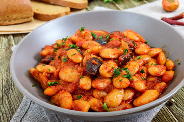 Stewed broad beans in tomato sauce with herbs and spices close-up, slices of rye bread on the wooden table. Lenten menu. Vegan dish.