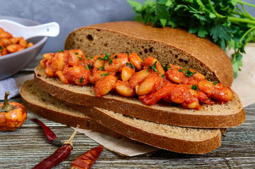 A piece of rye bread with beans. Stewed beans in tomato sauce with herbs and spices on the table. Lenten menu. Vegan dish.
