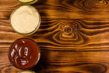 Different sauces in glass bowls on wooden table. Top view