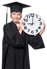 Portrait of a graduate girl student in a black graduation gown with hat, holding big clock - isolated on white background. Child back to school, educational and time concept.