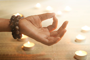 Woman hand practicing yoga and meditating on candle warm glowing background