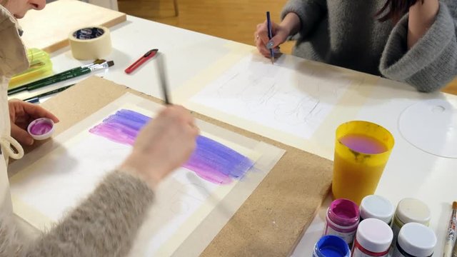 Two adult women paint with colored acrylic paints in an art school close up