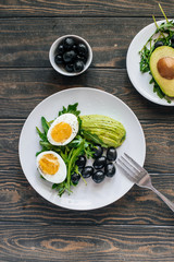 Healthy salad with arugula, avocado, egg and olives