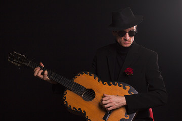 stylish guy in suit with guitar, on black background