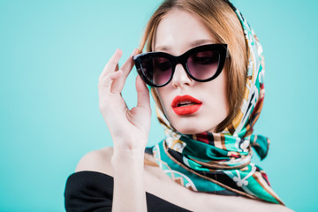 Portrait of a stylish woman posing in sunglasess and scarf on head, isolated on blue background. Horizontal.