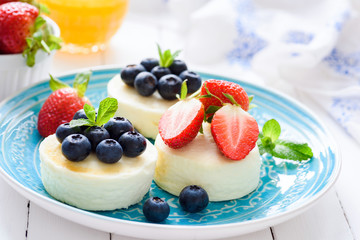 Mini cheesecakes with fresh strawberries and blueberries on blue plate, closeup view. Syrniki, cottage cheese pancakes