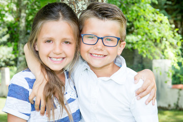 Portrait of adorable brother and sister smile and laugh together while sitting outdoors with glasses