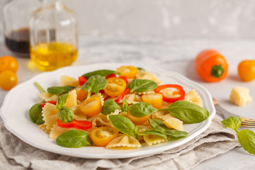 Italian pasta farfalle salad with vegetables, basil and spinach in a white plate. Vegan food concept. Light background