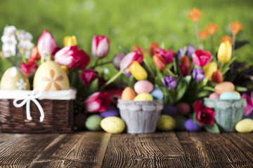Easter background. Rustic wooden table. Tulips and spring flowers. Easter eggs. Colorful bokeh. Place for typography. 