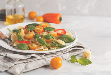 Italian pasta farfalle salad with vegetables, basil and spinach in a white plate. Vegan food concept. Light background, copy space