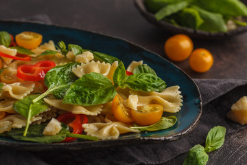 Italian pasta farfalle salad with vegetables and spinach in a beautiful vintage plate. Dark background