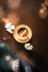 Overhead latter art coffee in a yellow cup with flowers on a wooden table at the hipster coffee shop. Toned. Copyspace 