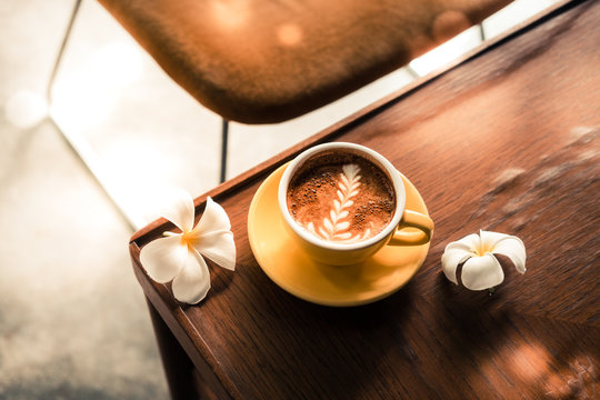 Latte Art Specialty Coffee In A Yellow Cup With Flowers From Above On A Wooden Table At The Hipster Coffee Shop. Vintage Color Filter Effect. Copyspace 