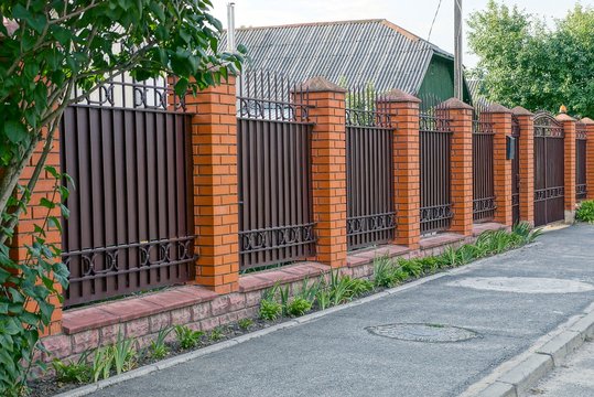 Part of a private iron brown fence and gate at the green grass in the street 