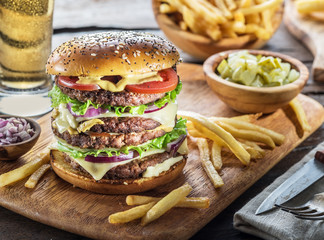 Big hamburger and French fries on the wooden tray.