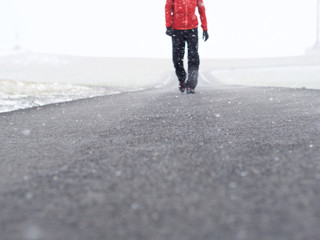Person mit roter Jacke von vorne läuft  im Schneesturm, Schneefall