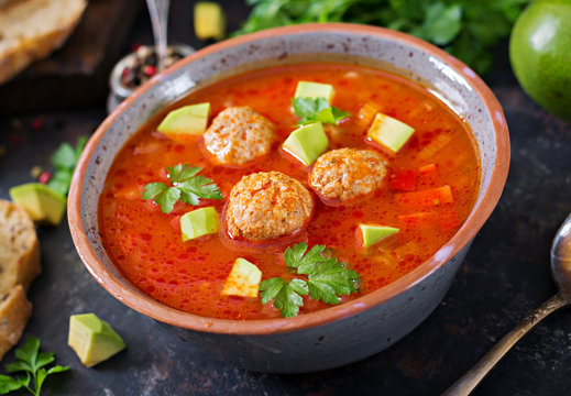 Spicy tomato soup with meatballs and vegetables. Served with avocado and parsley. Healthy dinner