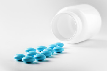 Medical blue pills and white bottle on white light background. Concept of healthcare and medicine.