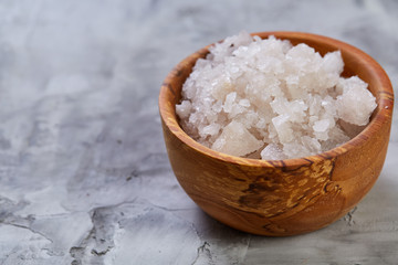 Large white sea salt in a natural wooden bowl on white background, top view, close-up, selective focus