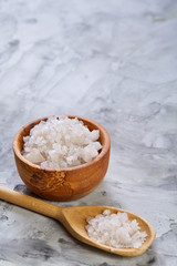 Crystal sea salt in a wooden spoon on dark background, top view, close-up, selective focus.