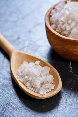 Crystal sea salt in a wooden spoon on dark background, top view, close-up, selective focus.